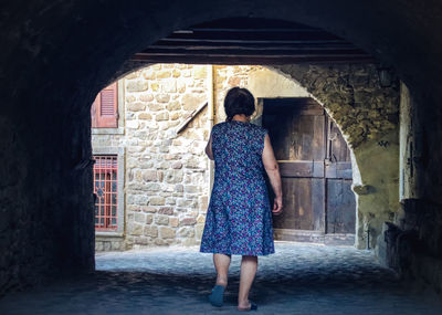 Rear view of woman walking on footpath below arch