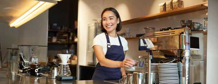 Portrait of young woman looking away while standing in cafe