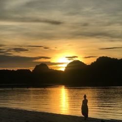 Silhouette man looking at lake against sky during sunset