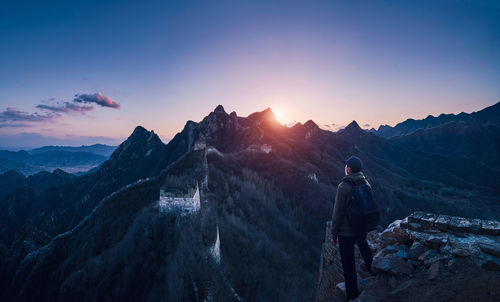 Rear view of man standing on mountain against sky during sunset