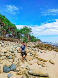 Full length of man on rock at beach against sky