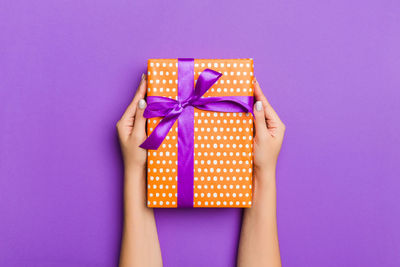 Cropped hands of woman holding gift against purple background