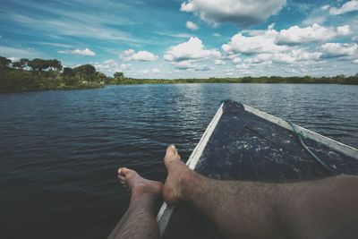 Low section of man relaxing on boat in lake against sky