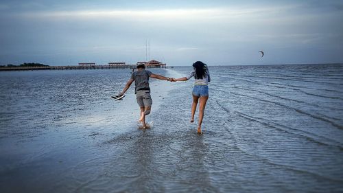 Rear view of friends standing on sea against sky