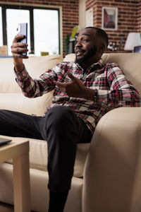 Young man using mobile phone while sitting on sofa at home