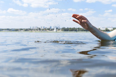Cropped hand of person swimming in lake against sky
