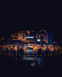 Illuminated buildings by river against sky at night