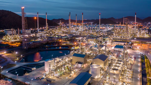 High angle view of refinery illuminated city against sky at night