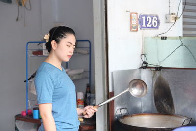 Side view of young woman having food in kitchen