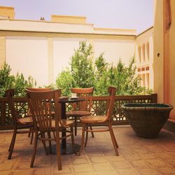 Chairs and table by potted plants against house