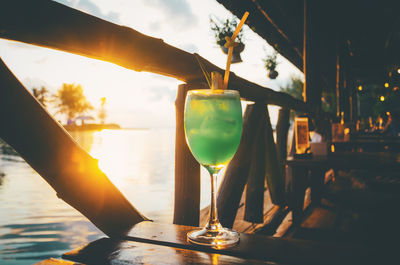 Close-up of hand holding wine glass against sunset sky