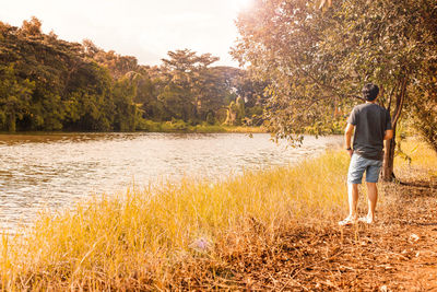 Rear view of man standing by lake in forest during autumn