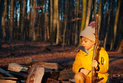 Cute girl sitting on wooden log in forest