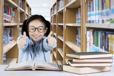 Portrait of smiling girl showing thumbs up in library