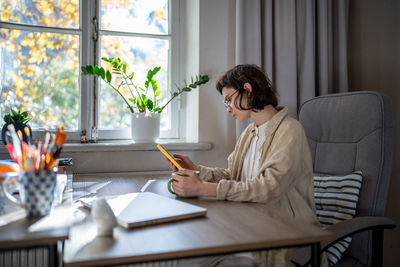 Side view of young woman using laptop at table