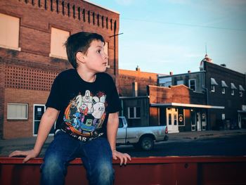 Young man looking away while standing on house against sky