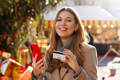 Woman holding credit card and smartphone in her hands looking at camera at the christmas markets