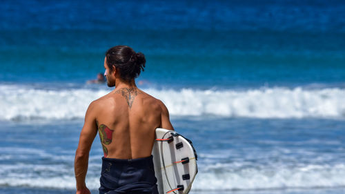 Rear view of man holding surfboard while looking away in sea