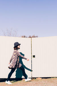 Full length side view of woman walking by gate on sunny day