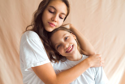 Sisters hugging on beige color textile background