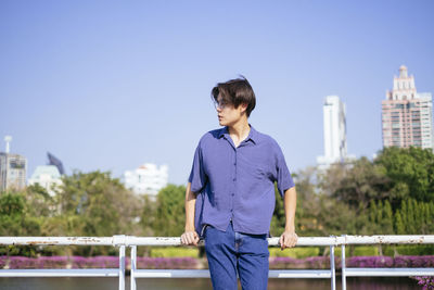 Full length of teenage girl standing on railing against blue sky