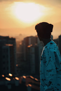 Silhouette man looking at city against sky during sunset