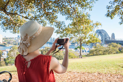 Rear view of woman photographing bridge while standing at park