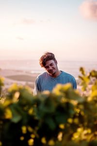 Portrait of young man winking while standing against sea during sunset