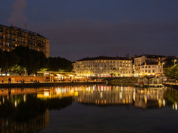 Illuminated buildings by river against sky at night