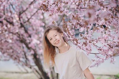 Portrait of young woman standing against cherry blossom tree