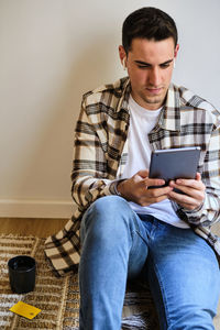 Young man shopping and paying online on digital tablet with credit card while relaxing at home listening music with earphones.