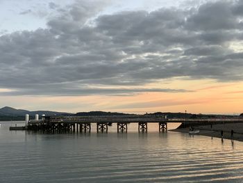 Pier over river against sky during sunset