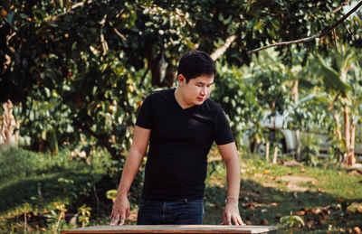 Young man standing by table against trees