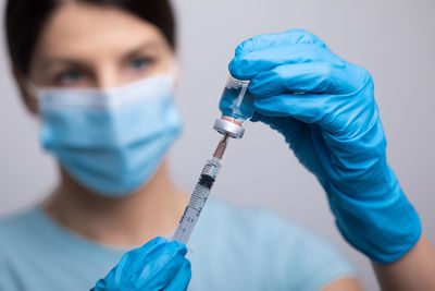 Doctor wearing mas holding vial and syringe against gray background