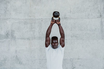 Young sportsman exercising with kettle bell against white wall