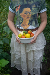Midsection of woman carrying vegetables in container on field