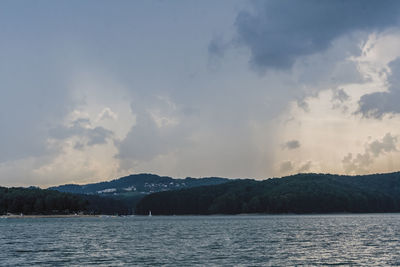 Scenic view of sea and mountains against cloudy sky