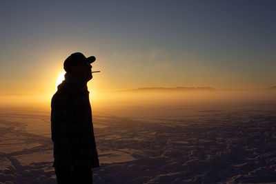 Silhouette man standing on snow covered land against sky during sunset
