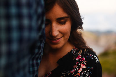 Happy peaceful young hispanic female cuddling to unrecognizable beloved man while spending romantic time together in nature