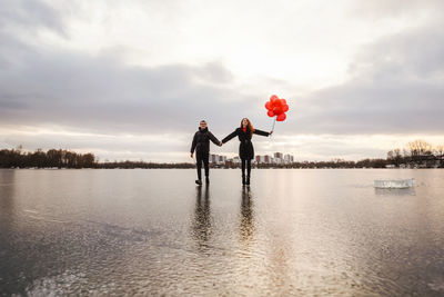 Couple standing by lake against sky