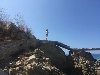 Low angle view of man climbing on mountain against clear blue sky