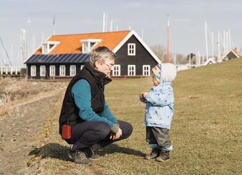 Grandfather with granddaughter crouching on field against house