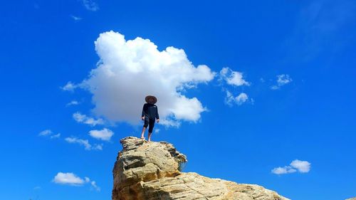 Low angle view of man standing on rock against blue sky