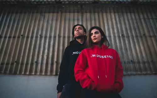 Young couple looking away while standing against corrugated wall