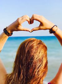 Rear view of woman gesturing heart shape against sea