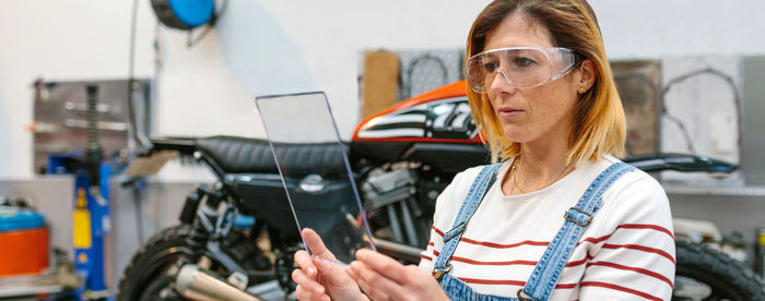 Female mechanic with security glasses holding transparent tablet