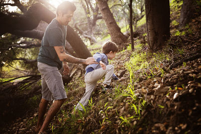 Man assisting son in climbing at forest