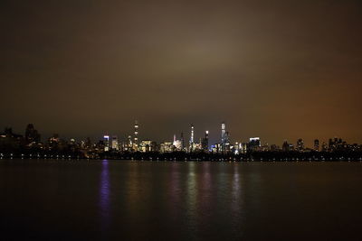 Illuminated buildings by sea against sky at night