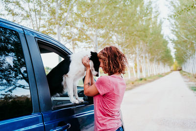 Side view of woman holding dog through car window