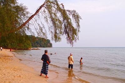 Rear view of people on beach against sky